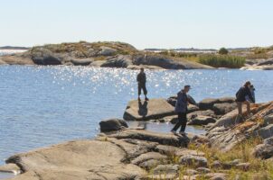 Människor går längs vattnet på en ö och havet glittrar i bakgrunden