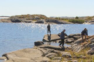 Människor går längs vattnet på en ö och havet glittrar i bakgrunden