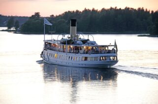 The steamship Blidösund sails in calm waters at sunset.