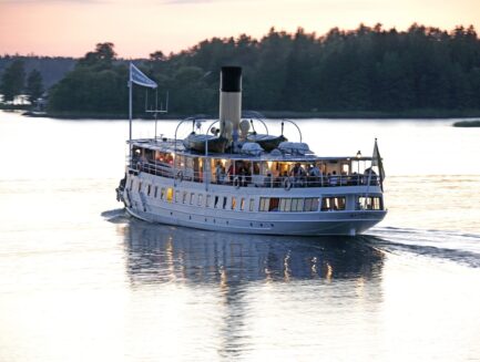 The steamship Blidösund sails in calm waters at sunset.